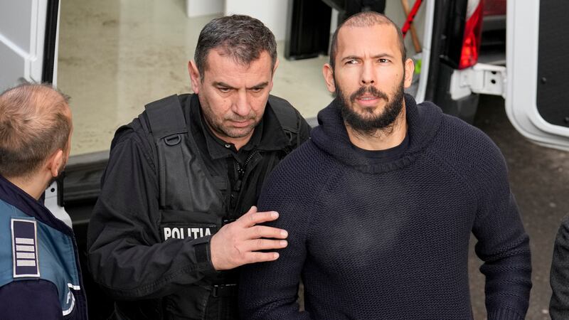 Police officers escort Andrew Tate, right, handcuffed to his brother Tristan Tate, to the...
